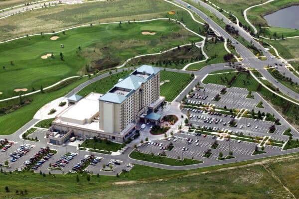 Multi-story hotel complex anchors a landscaped campus, surrounded by dozens of parked cars in extensive parking lots, adjacent to manicured golf-course fairways, winding paths, and intersecting roads.