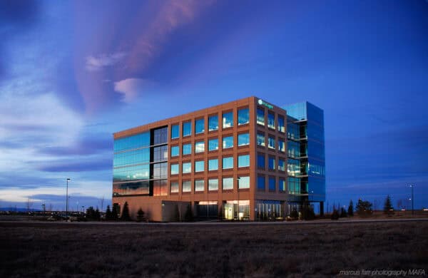 A glass office building reflects sunset, its lit windows glowing; it stands on a grassy plain under a deep blue dusk sky with sweeping clouds. Visible text: marcus farr photography MAFA
