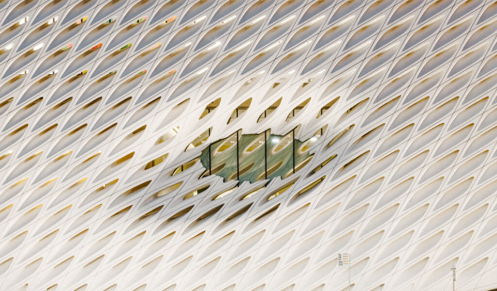 White diamond-patterned lattice facade forms a central oval opening exposing glass panels; behind them a green-lit interior corridor and stairs are visible amid the repeating perforated exterior.