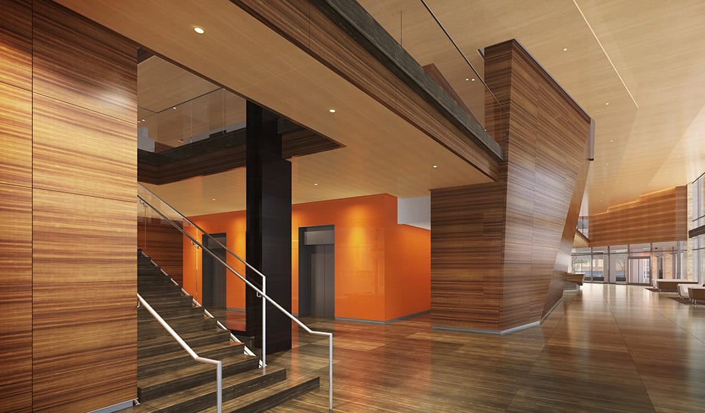 Central dark-wood staircase ascends to a mezzanine; stainless handrails guide upward. Surrounding space: a spacious, modern lobby with warm wood paneling, polished floors, orange elevator wall and large windows.