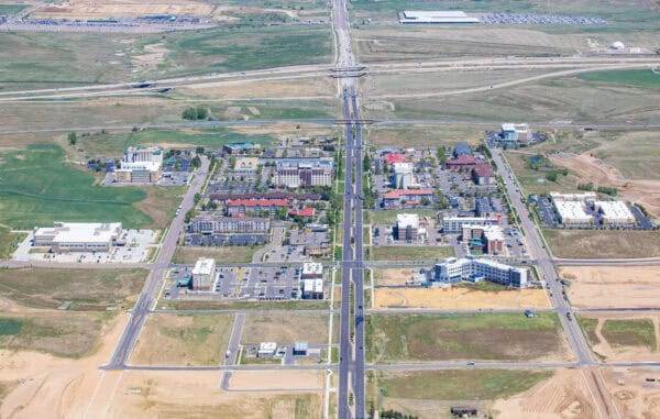 Wide central boulevard runs north–south through a grid of low-rise commercial and residential buildings, parking lots, and vacant lots, crossing highway overpasses with open fields stretching beyond.