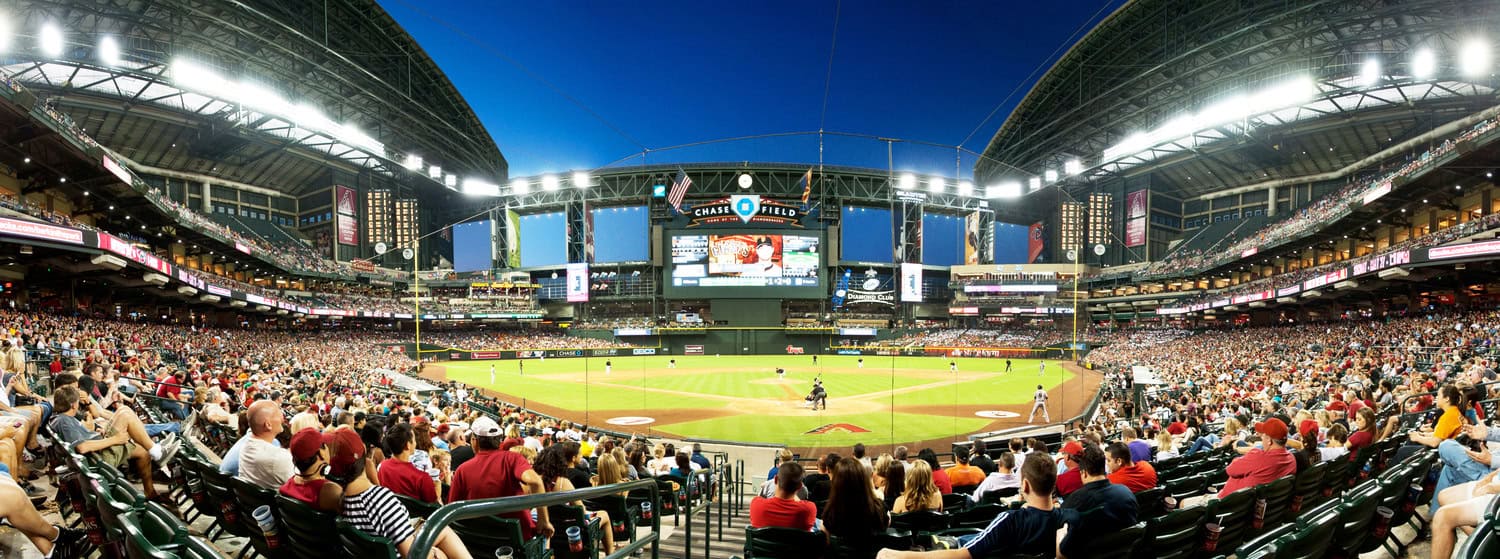 Baseball field hosting a game: a batter at the plate and fielders positioned while a large crowd watches in a brightly lit, roofed stadium with a central video scoreboard.

Visible text (legible): "CHASE FIELD", "DIAMOND CLUB"