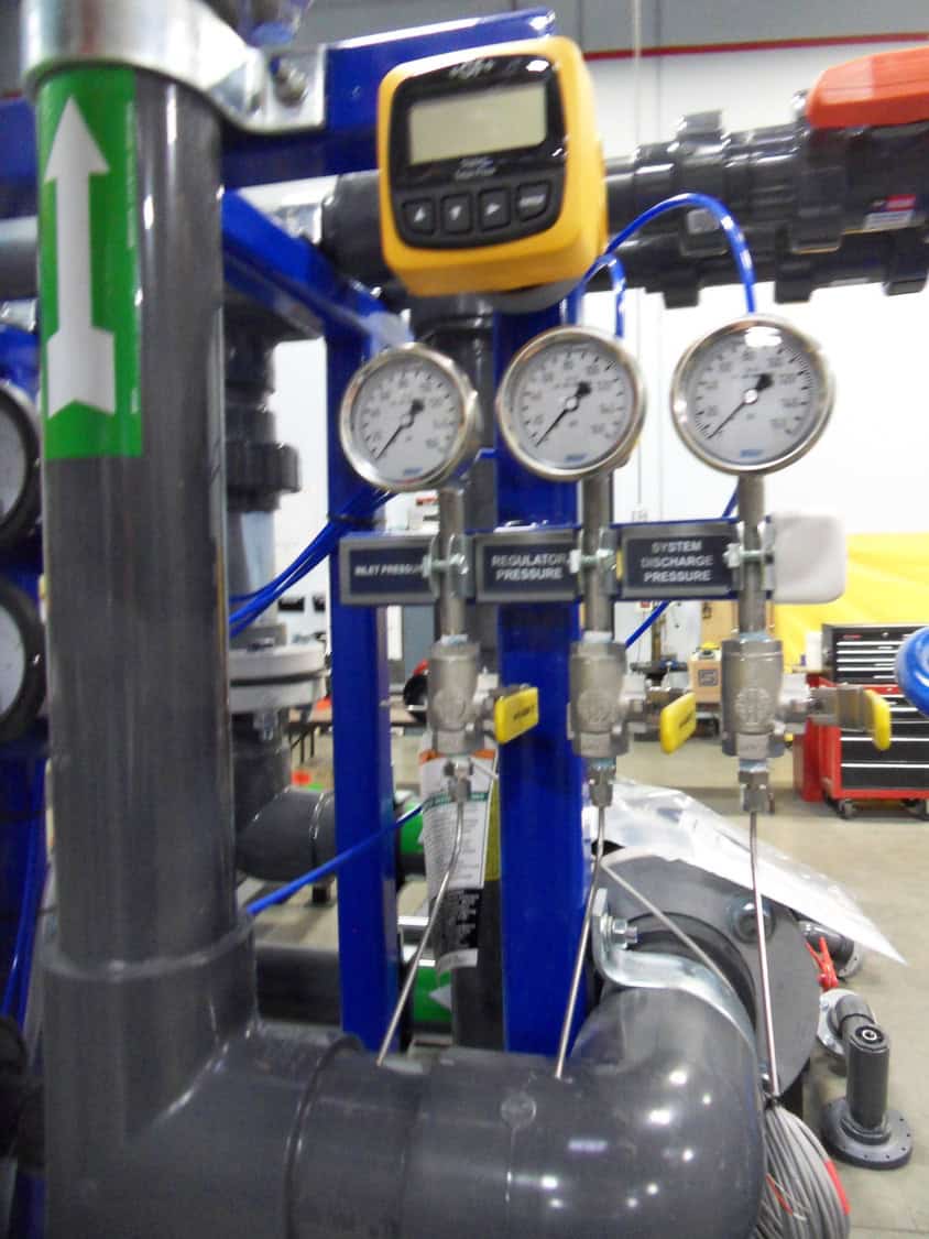 Three pressure gauges monitor pipeline flow, mounted above brass valves and a digital meter on a blue frame amid large PVC piping in an industrial workshop.

Transcription:
- INLET PRESSURE
- REGULATOR PRESSURE
- SYSTEM DISCHARGE PRESSURE
- (green label with upward arrow)