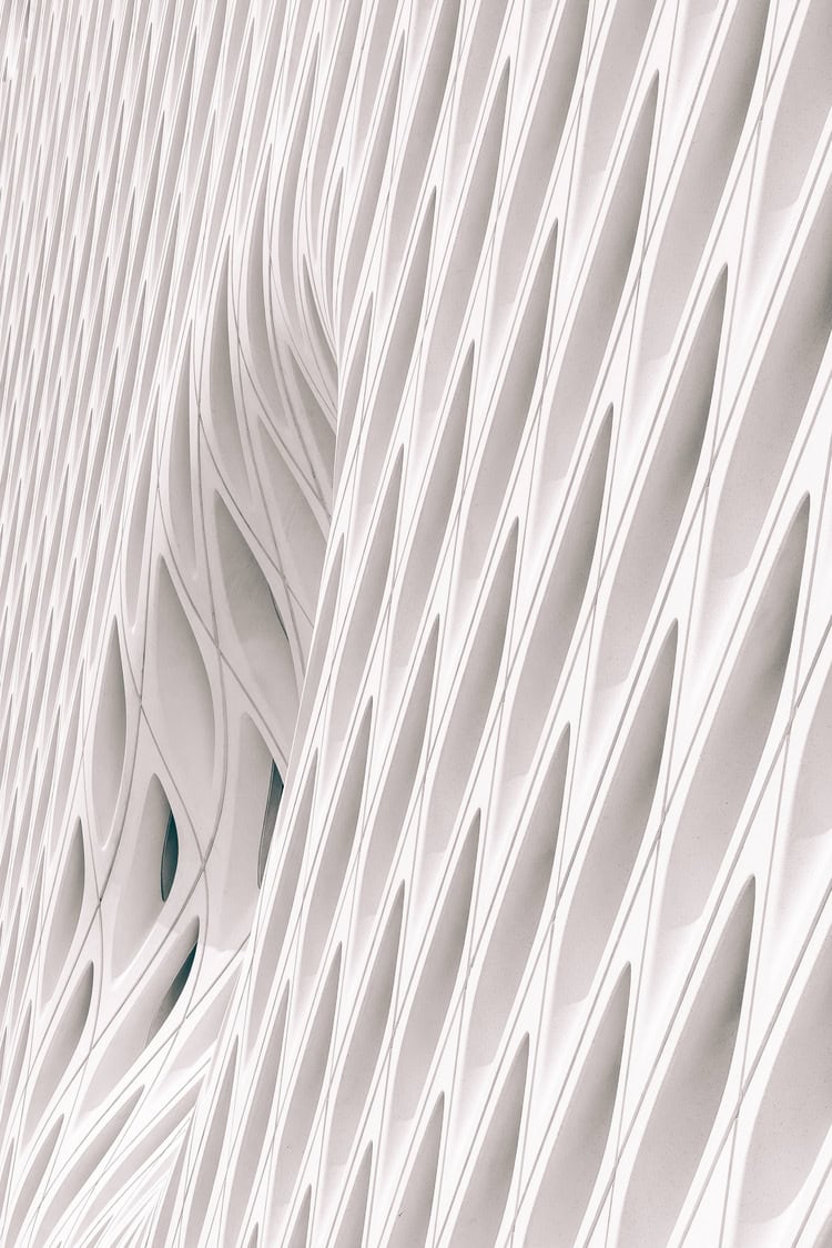 White architectural façade ripples in a diagonal, honeycomb-like pattern of elongated diamond openings, forming a curving, repetitive lattice across a high-rise exterior.