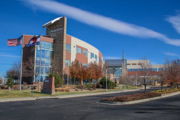 Platte Valley Medical Center building stands framed by American and Colorado flags, with autumn trees and a curved driveway under a clear blue sky.

Text in image: "Platte Valley MEDICAL CENTER SCL Health"
