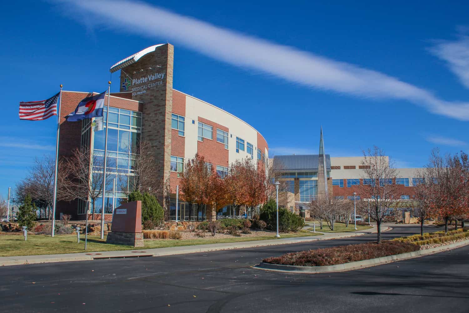 Platte Valley Medical Center building stands framed by American and Colorado flags, with autumn trees and a curved driveway under a clear blue sky.

Text in image: "Platte Valley MEDICAL CENTER SCL Health"