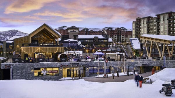 A wooden lodge labeled "THE RANGE" glows with string lights as people gather on a snowy plaza in front of multi-story resort buildings at sunset.

Text visible: THE RANGE; SKI PATROL; Steamboat; YAMAHA; SEASONAL LOCKERS & STORAGE; URGENT CARE • SKI PATROL • RESTROOMS • SKI VALET • LOCKERS