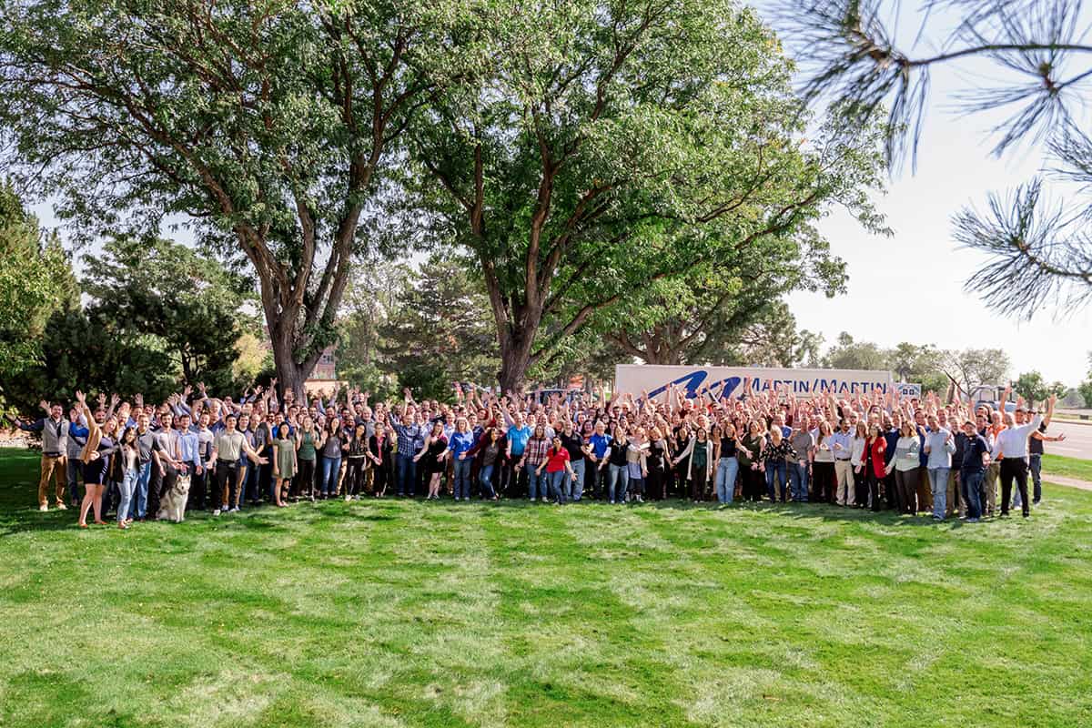 Large crowd of people waving and smiling on a grassy lawn under tall trees, gathered beside a truck labeled "MARTIN/MARTIN".